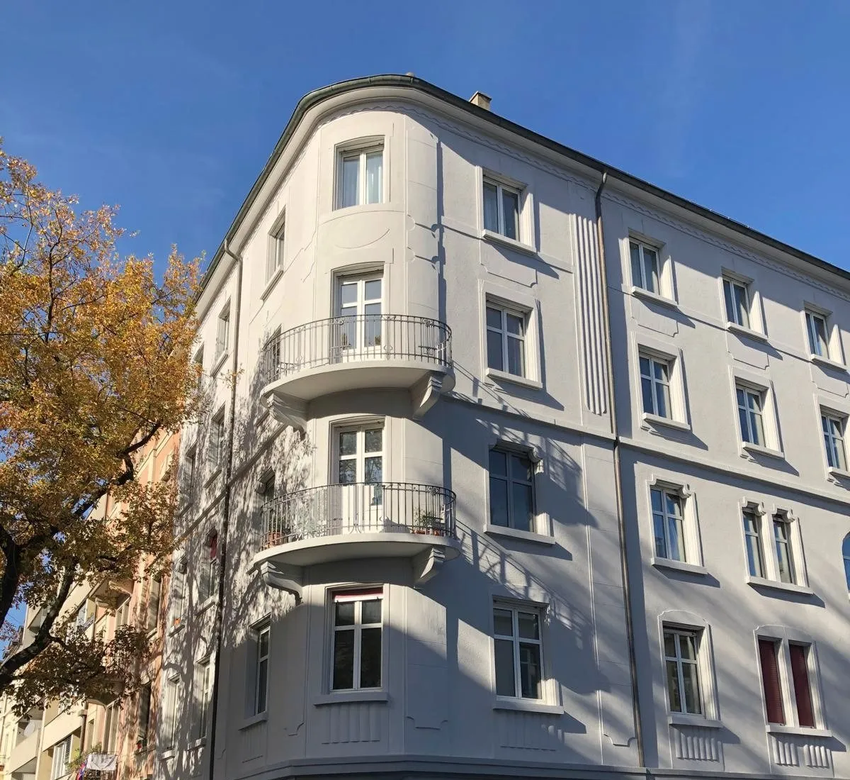 Eckhaus mit hellgrauer Fassade und runden Balkonen in der Herbstsonne