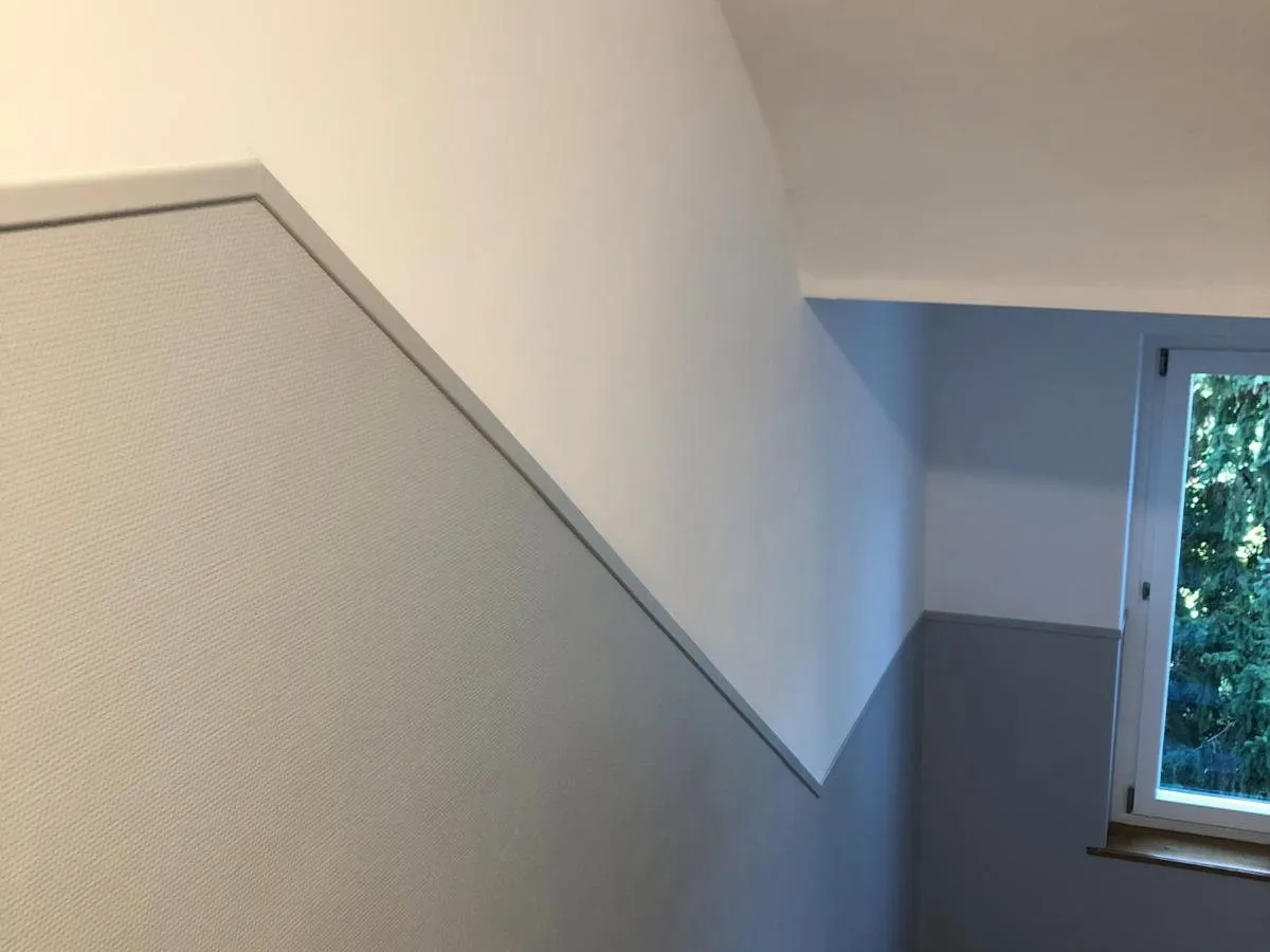 Treppenhauswand mit hellgrauem unterem und weissem oberem Wandteil, getrennt durch eine Abschlussleiste